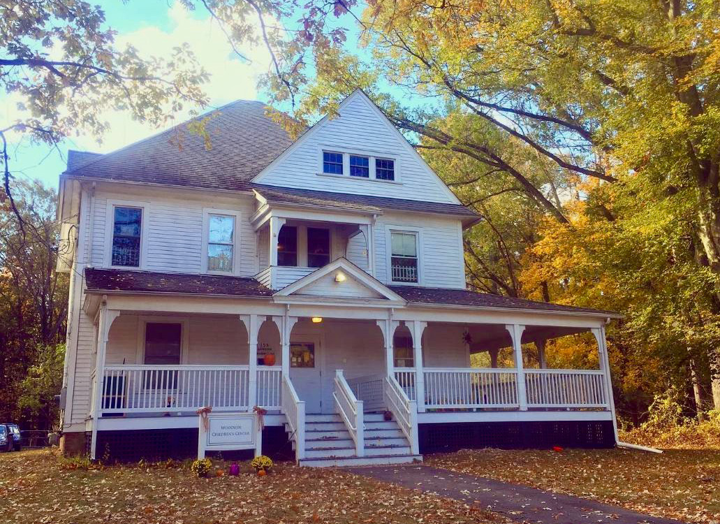 A large two-story white house with a front porch surrounded by fall foliage.