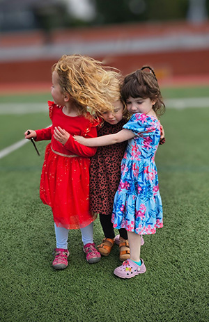 Three young girls hugging each other standing outside on a green lawn