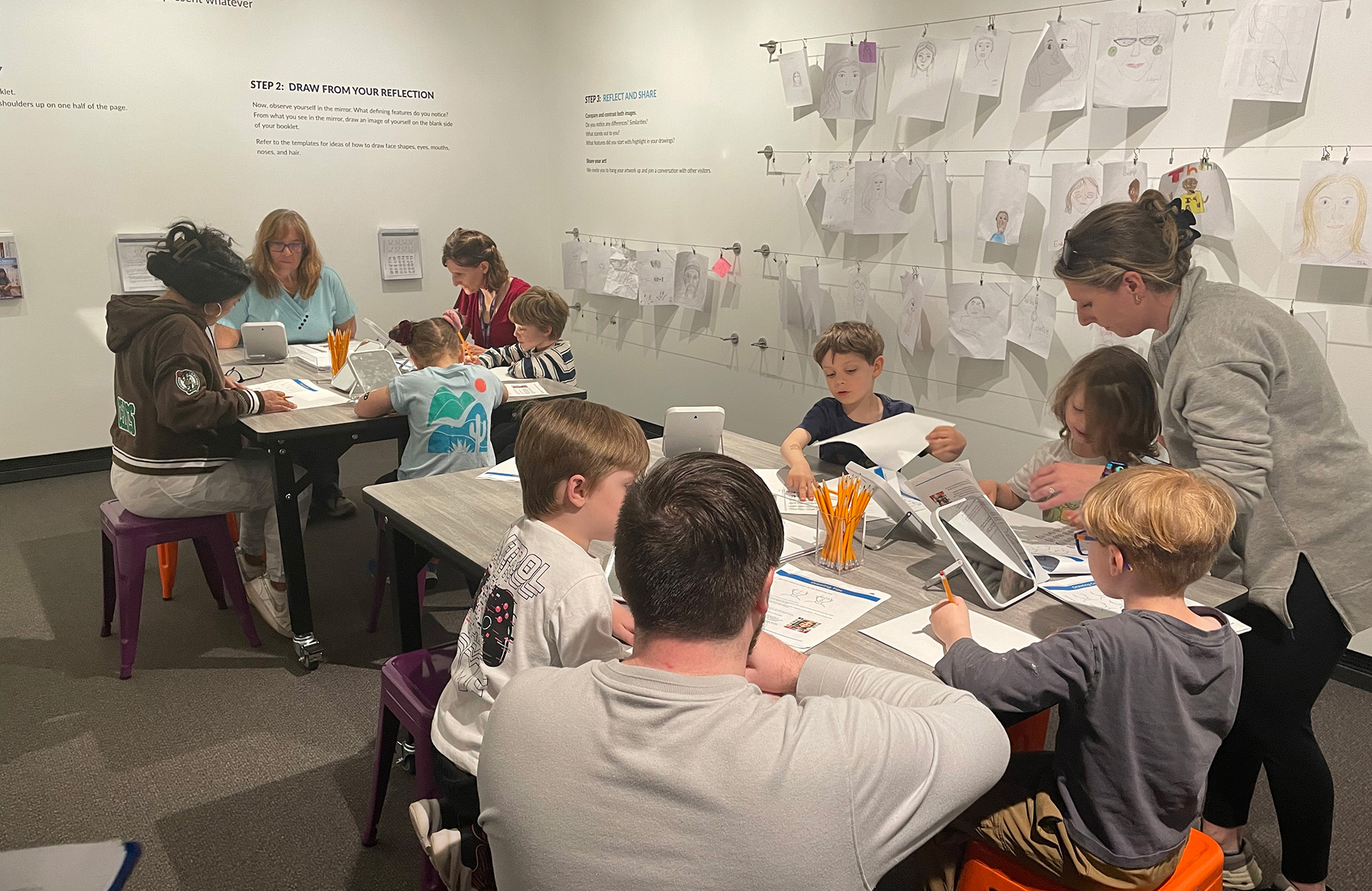 Children working at tables in a museum with children's art displayed on the walls around them.